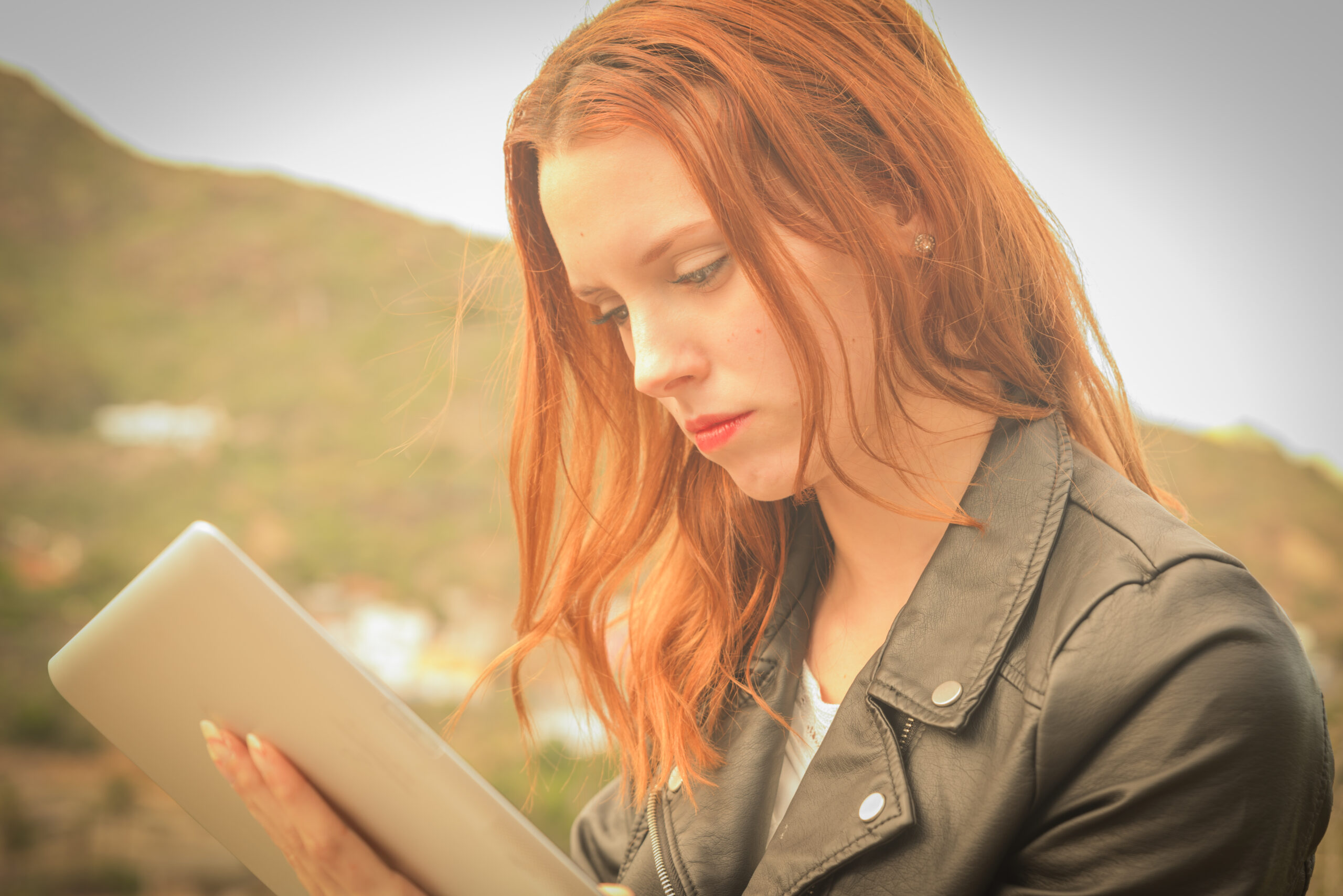 Millennial joven de pelo rojo disfrutando de videochat al aire libre en tiempos de crisis y encierro, usando auriculares y movil o tablet para conectarse con el mundo.